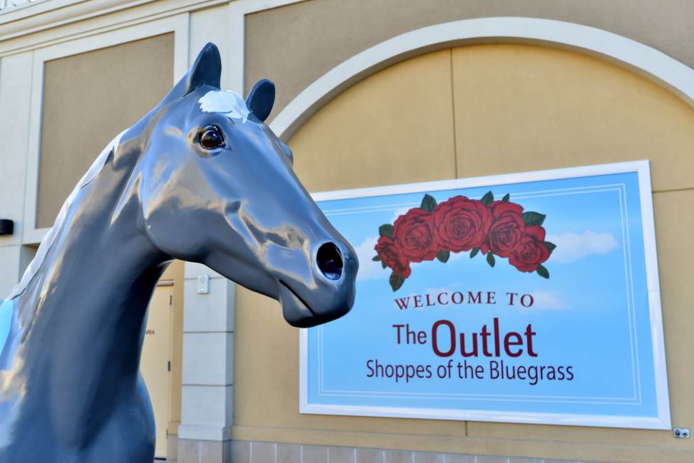 A statue of a horse stands in front of a sign that reads, "Welcome to the Outlet Shoppes of the Bluegrass"