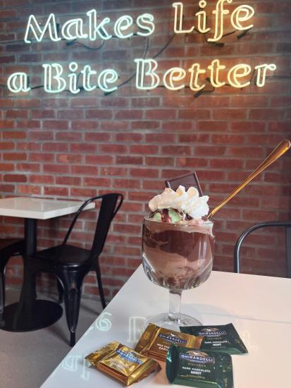 A Ghirardelli chocolate ice cream sundae with whipped cream sits in a glass dish on a tabletop.