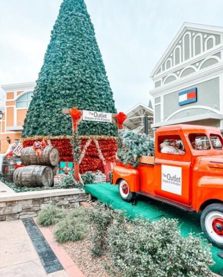 An antique red truck is parked on a decorated pedestal with a massive Christmas tree and decorations behind it.