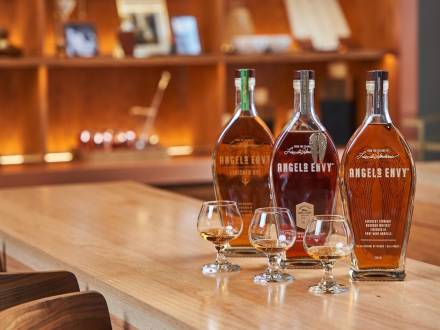 Three bottles of Angel's Envy sit on a bar top alongside three tasting glasses.