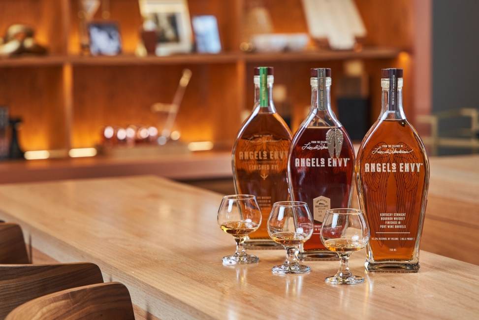 Three bottles of Angel's Envy sit on a bar top alongside three tasting glasses.