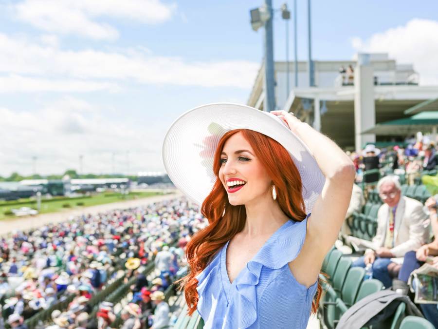 A red-headed woman in Derby hat and attire in the stands of Churchill Downs