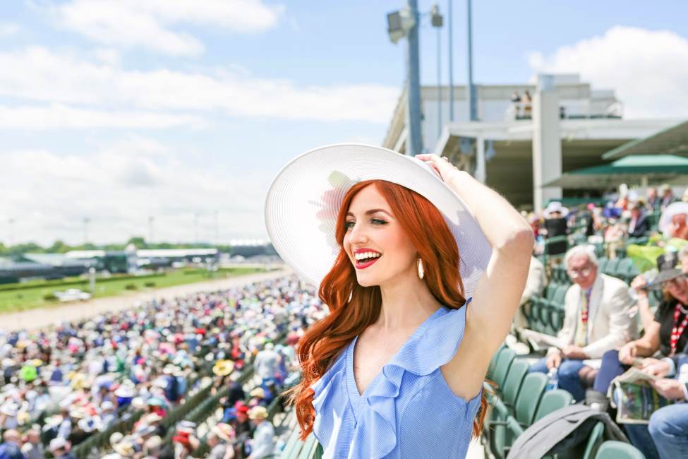 A red-headed woman in Derby hat and attire in the stands of Churchill Downs