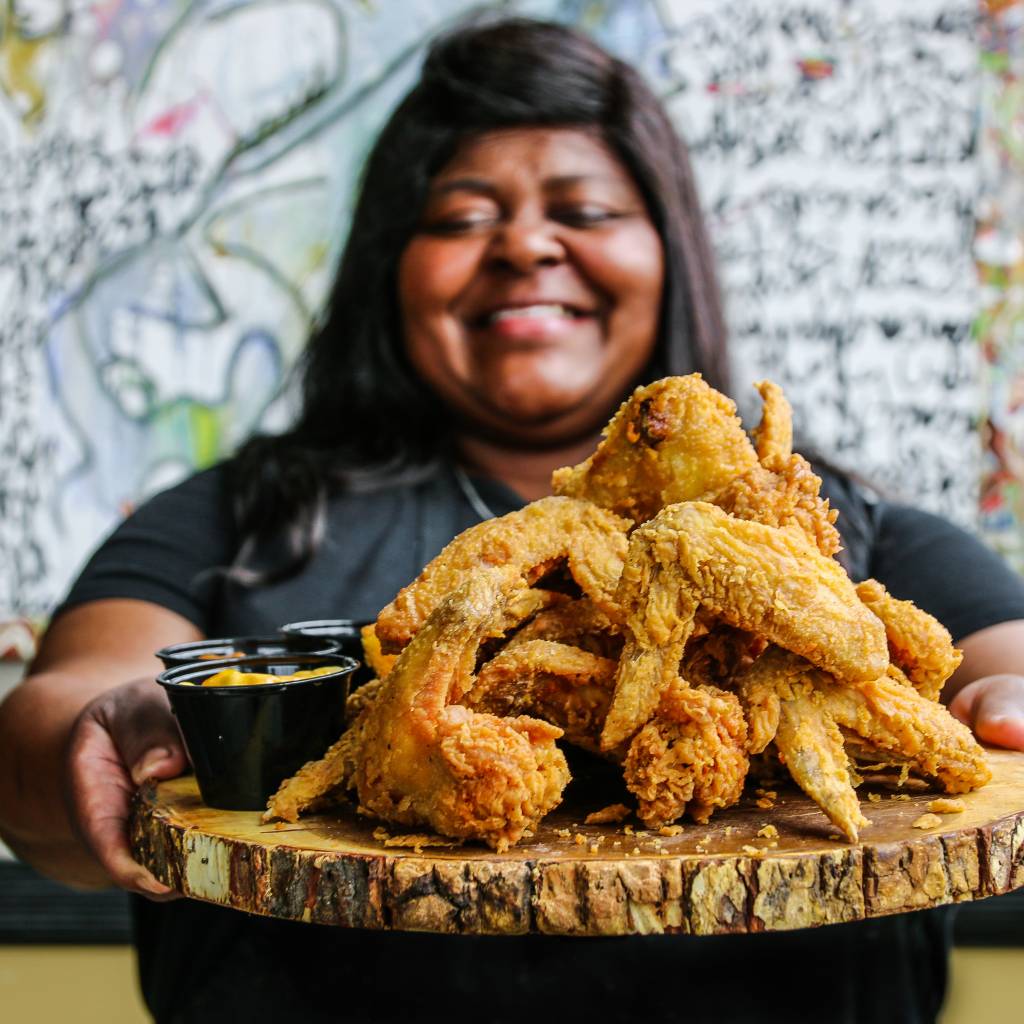 a smiling woman holding a tray of fried chicken from LuCretia's Kitchen, a soul food restaurant in Louisville