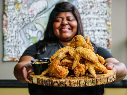 a smiling woman holding a tray of fried chicken from LuCretia's Kitchen, a soul food restaurant in Louisville