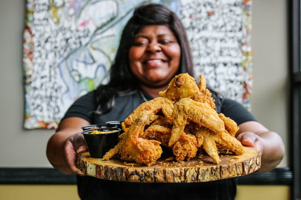 a smiling woman holding a tray of fried chicken from LuCretia's Kitchen, a soul food restaurant in Louisville