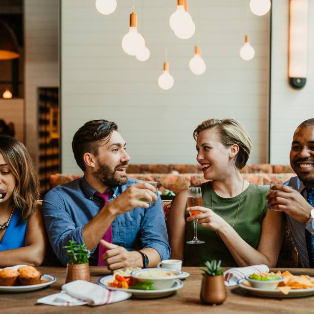 Photo of two couples sitting at a restaurant table with food in front of them and cocktails in hand.