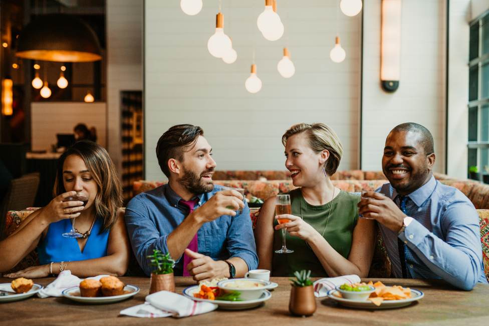 Photo of two couples sitting at a restaurant table with food in front of them and cocktails in hand.