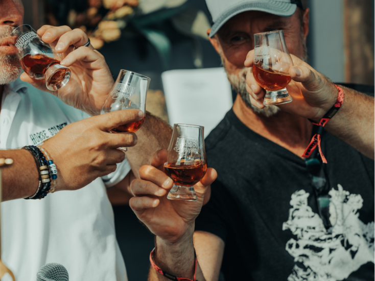 Men raising glasses of bourbon at Bourbon & Beyond, showcasing camaraderie and celebration with amber drinks in hand.
