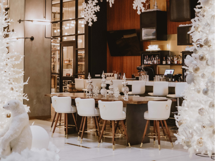 Elegant hotel bar decorated for the holidays with white trees, ornaments, snowflakes, and cozy seating around a wood table.