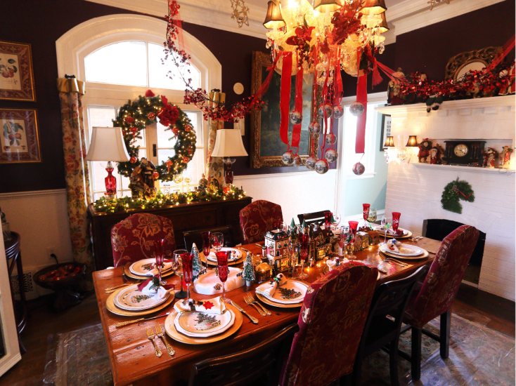 A cozy dining room decorated for Christmas with garlands, wreaths, red ribbons, and a festive table set for a holiday meal.