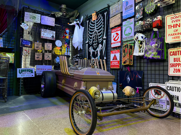 Halloween-themed display at Caufields Novelty featuring a coffin car, skeleton decor, spooky signs, and a costume wall.