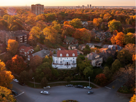 Aerial view of a Louisville neighborhood with fall foliage, historic homes, and city skyline in the distance at sunset.
