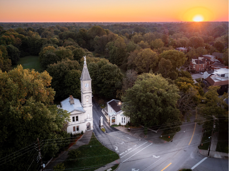 Aerial view of Cave Hill Cemetery’s historic entrance and clock tower surrounded by fall foliage at sunset in Louisville, KY.