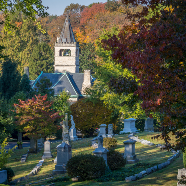 Cave Hill Cemetery in Louisville with historic monuments, colorful autumn trees, and a stone chapel tower in the background.