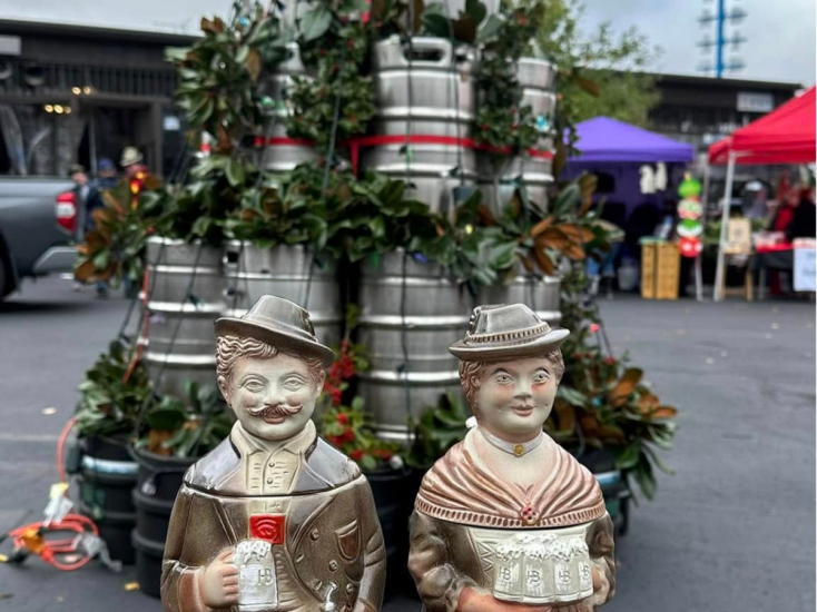 Ceramic beer steins shaped like a man and woman stand in front of a festive keg Christmas tree at German American Club.