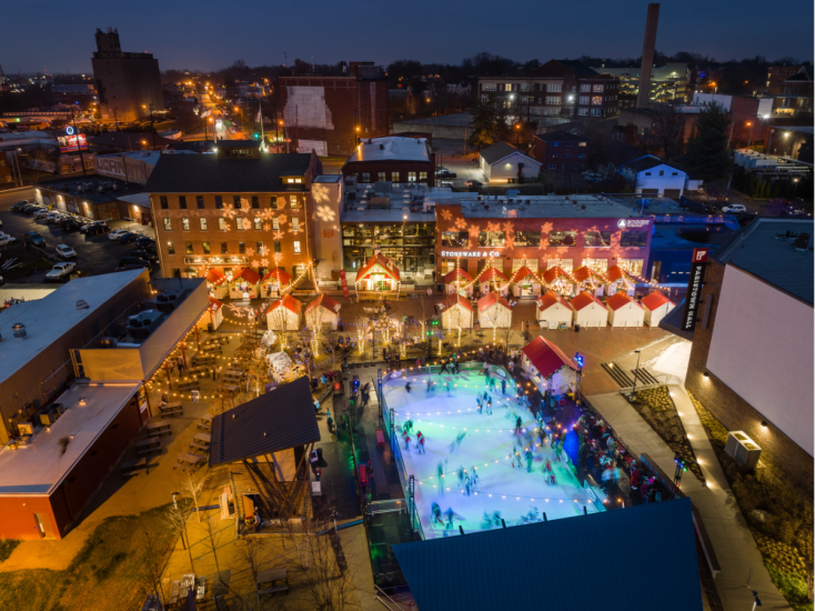 Aerial view of Fête de Noël at Paristown featuring an outdoor ice rink, festive lights, and holiday market huts at night.