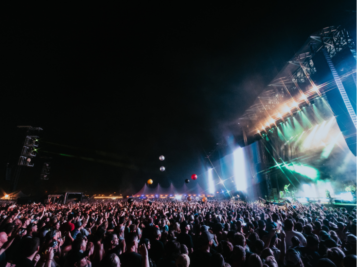 A massive crowd rocks out under stage lights at Louisville’s Louder Than Life music festival during a night performance.